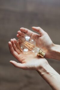 A pair of hands holding a large unlit bulb. Write Good.