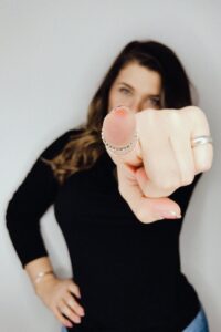 A woman pointing at the camera intensely. Your writing sucks? Perish the thought. You are greatness.