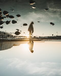 A woman reflected in water walking on the beach. God of Darkness?