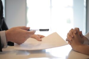 A person with pen and paper handing them solemnly to another person. What Should I Write About?