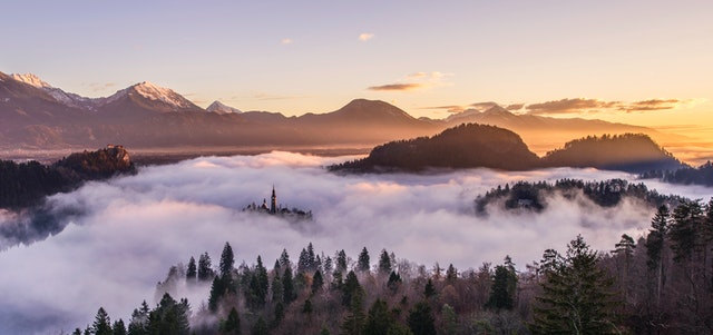 A cloud covered valley covered with trees and surrounded by mountains. Show Don't Tell.
