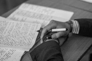 A pair of hands holding a pen with numerous sheaves of handwritten pages surrounding. What Should I Write About? 