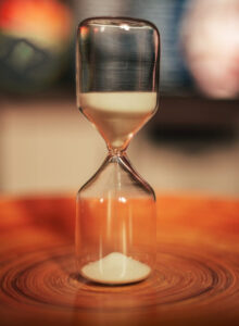 A small rustic hourglass placed upon a wooden desk.